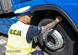 Policjant drogówki sprawdza oponę w pojeździe ciężarowym.