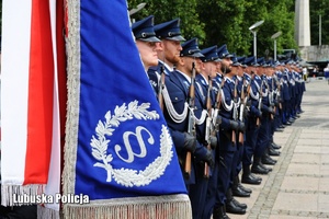 Sztandar policyjny, a w tle policjanci stojący w szeregu.