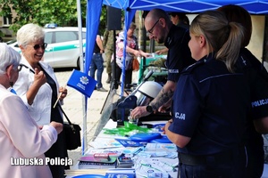 Policjanci na stoisku profilaktycznym rozmawiają ze starszymi osobami.