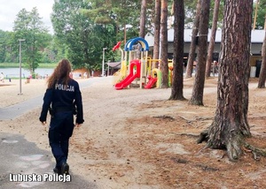 Policjantka idąca przez teren ośrodka wypoczynkowego nad jeziorem.