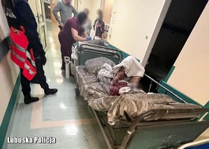 Policjantka przy łóżku pacjenta, a obok inne osoby.