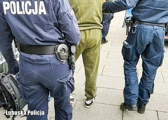 Policjanci prowadzą zatrzymanego mężczyznę do radiowozu.