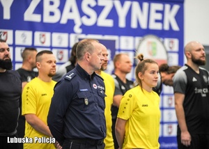 Policjant stojący w rzędzie przy zawodnikach - uczestnikach turnieju piłkarskiego.