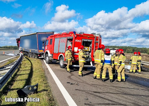 Strażacy stojący przy wozie straży pożarnej, a za nimi ciężarówka, która uczestniczyła w zdarzeniu drogowym.