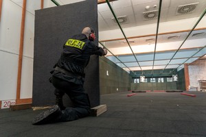 Policjant strzela do tarczy zza zasłony.