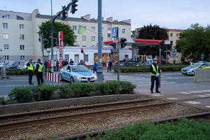 Dwaj policjanci ruchu drogowego i strażnik miejski obserwują teren skrzyżowania i torowiska