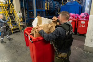 policjant wrzuca papierowy worek do kontenera na śmieci