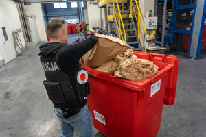 policjant wrzuca papierowy worek do kontenera na śmieci