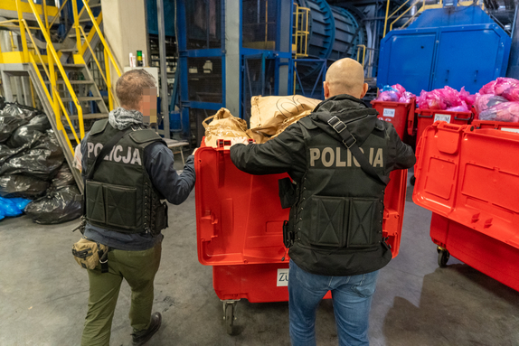 policjanci pchają kontener na śmieci w stronę pieca