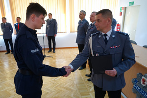 Komendant przekazuje akt ślubowania policjantowi.