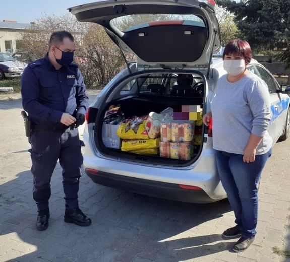 Karma zapakowana do bagażnika radiowozu. Przy aucie stoi policjant oraz osoba cywilna.