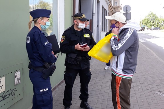 Policjantka i strażnik miejski wręczają mężczyźnie maseczkę ochronną