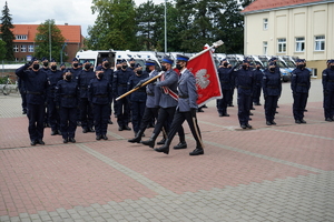 Poczet sztandarowy maszeruje przed szeregiem policjantów wstępujących do służby.