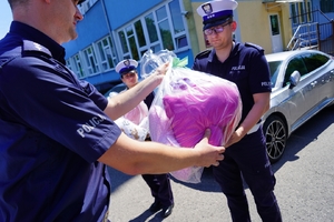 Policjant przekazuje maskotki innemu policjantowi