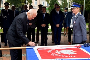 emerytowany policjant przybija młoteczkiem gwóźdź do sztandaru