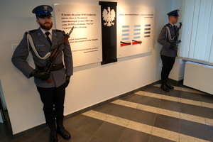 dwaj umundurowani na galowo policjanci z karabinkiem stoją przy tablicy pamięci