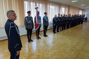 Odchodzący na emeryturę komendant stoi na tle pocztu sztandarowego i innych policjantów