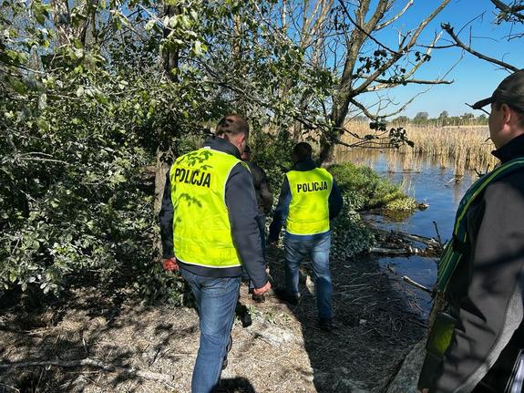 policjanci wraz z zatrzymanym mężczyzną idą brzegiem rzeki