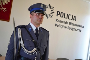 Policjant stoi przy ścianie na której widać napis Policja Komenda Wojewódzka Policji w Bydgoszczy