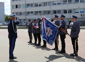 Szef policji salutuje przed pocztem sztandarowym.