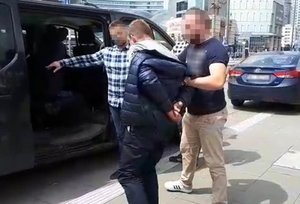 Policjanci wprowadzają zatrzymanego mężczyznę do radiowozu