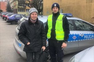 policjant ruchu drogowego stoi wraz ze starszą panią na tle radiowozu.