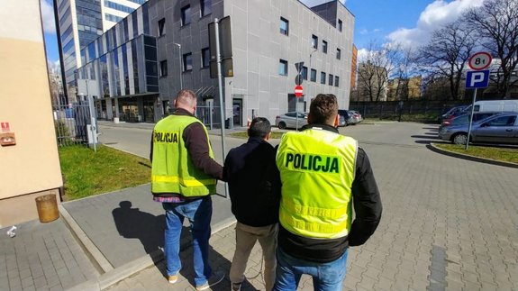 Dwaj policjanci w kamizelkach odblaskowych z napisem policja prowadza zatrzymanego.