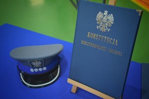 Sala gimnastyczna Oddziału Prewencji Policji w Łodzi, uroczystość ślubowania policjantów, stolik przykryty niebieskim suknem, na stoliku po lewej stronie czapka nadkomisarza policji, po prawej stronie Konstytucja Rzeczypospolitej Polskiej na stojaku.