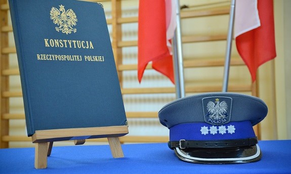 Na stole stoi Konstytucja RP po prawej leży oficerska czapka policyjna.