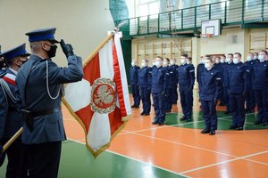 Sala gimnastyczna Oddziału Prewencji Policji w Łodzi. Uroczystość ślubowania policjantów. poczet sztandarowy, w tle stojący nowo przyjęci policjanci.