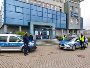 Radiowozy i policjanci na tle komendy.