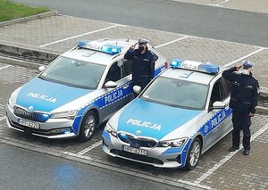 Dwa radiowozy i policjanci oddają honor.