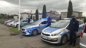 Kilka oznakowanych radiowozów obok policjanci.