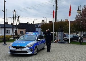 Radiowóz i obok policjant. W tle maszt z flagą.