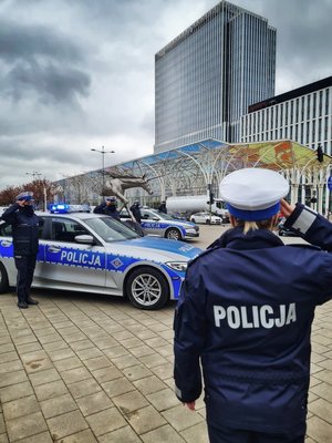 Policjantka stoi tyłem i salutuje, w tle inne radiowozy i policjanci.