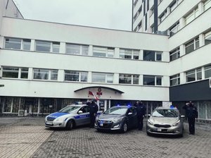 Trzy radiowozy, a obok policjanci, przed komendą policji.