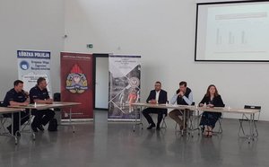 za dwoma stolikami prezydialnymi siedzi dwóch policjantów i troje cywili , w tym wojewoda, na ścianie wyświetlana jest prezentacja