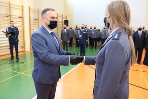 Sala gimnastyczna Oddziału Prewencji Policji w Łodzi, uroczystość ślubowania nowo przyjętych policjantów, wicemarszałek wręcza kluczyki policjantce.