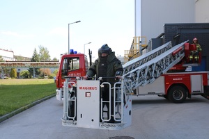 Policjant w stroju pirotechnicznym stoi w koszu na drabinie strażackiej.