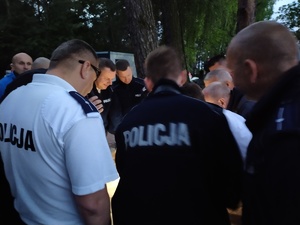 Policjanci i inne służby stoją w kręgu na odprawie do ćwiczeń.