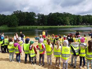 Dzieci w kamizelkach odblaskowych przyglądają się pokazowi na plaży.