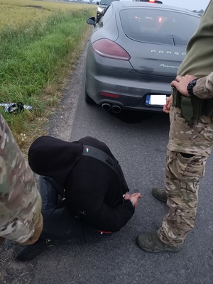 Policjant stoi z zatrzymanym, w tle skradziony samochód.