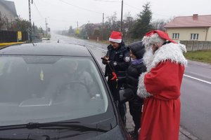 Policjanci z Mikołajem stoją przy zatrzymanym na drodze aucie.