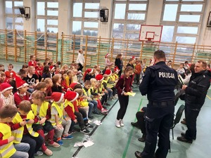Dzieci na sali gimnastycznej a przed nimi Mikołaj i policjanci.