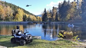 Zbiornik wodny w pobliżu zapory, policyjny śmigłowiec leci nad zaporą, na wodzie widoczna policyjna motorówka, na brzegu stoi quad.