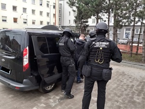 Policjanci z zatrzymanym wsiadają do auta.