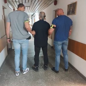 Korytarz, policjanci prowadza zatrzymanego.