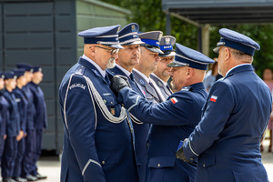 Policjant przypina medal policjantowi, pozostali policjanci stoją w szeregu.