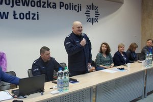 Sala konferencyjna goście i kierownictwo policji za stołem.