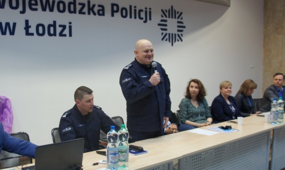 Sala konferencyjna goście i kierownictwo policji za stołem.